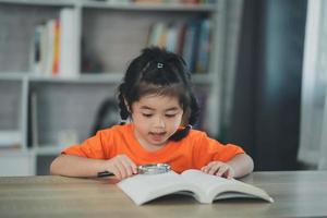 asiatisk bebis unge flicka innehav förstorande glas över bok och läsning bok utbildning, människor, barn och skola begrepp - Lycklig leende studerande flicka inlärning studerar. utbildning utveckling begrepp. foto