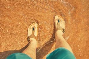 mäns fötter i sandaler på stranden. foto