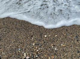 vågor av vatten i de hav och sand med små naturlig flerfärgad stenar på de stranden, små småsten på de strand. bakgrund, textur foto