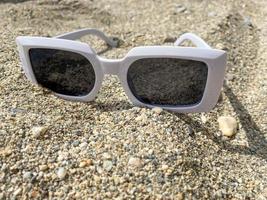 vit plast solglasögon för kvinnor på de gul sand av en strand i en värma östra tropisk Land sydlig paradis tillflykt foto