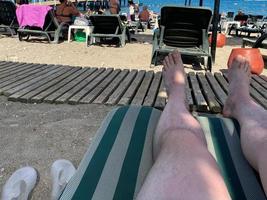 horisontell orientering av manlig fötter på en Sol vilstol utsikt ett oändlighet slå samman mot de hav, med Plats för text foto