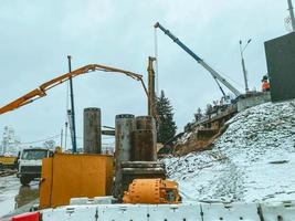 konstruktion av en ny bro i de stad Centrum. Utrustning Arbetar i de vinter- i de snö. en tung stor kran bär betong strukturer för de konstruktion av ett planskild foto