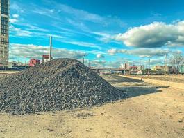 konstruktion webbplats. en mound av stenar och sand Nästa till lång hus under konstruktion. de bearbeta av byggnad ny flera våningar byggnader. stenar för konstruktion och asfalt om foto