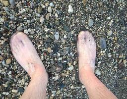 många stenar av annorlunda färger och former lögn på de strand. promenad på de rocks. textur med stenar. fötter i tofflor för simning och gående på småsten, skarp stenar på de strand foto