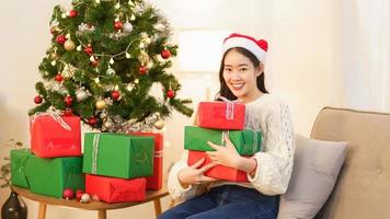 jul firande begrepp, ung asiatisk kvinna Sammanträde på de soffa och innehav jul gåvor foto