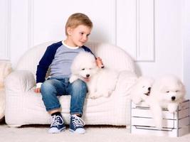 leende liten tre år gammal pojke spelar med vit valp av samojed i studio foto