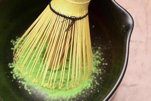 matcha grön te matlagning bearbeta i en svart skål med bambu vispa. organisk grön te matcha pulver. selektiv fokus. foto