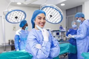 porträtt av kvinna kirurg stående i rörelse rum, redo till arbete på en patient. kvinna medicinsk arbetstagare kirurgisk enhetlig i drift teater. foto