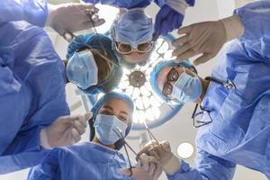 kirurger stående ovan av de patient innan kirurgi. multietnisk sjukvård arbetare utför kirurgi på patient på drift teater. foto