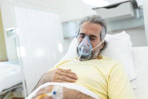 porträtt av pensionerad senior man andas långsamt med syre mask under coronavirus covid-19 utbrott. gammal sjuk man liggande i sjukhus säng, få behandling för dödligt infektion foto