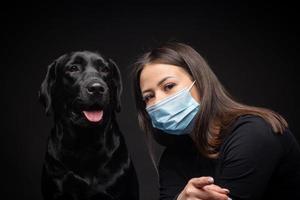 porträtt av en labrador retriever hund i en skyddande medicinsk mask med en kvinna ägare. foto