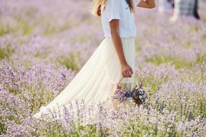 stänga upp se av kvinna i skön vit klänning den där använder sig av korg till samla lavendel- i de fält foto