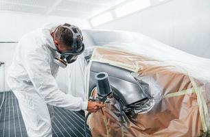 målning jobb i framsteg. caucasian bil reparatör i enhetlig Arbetar i garage foto