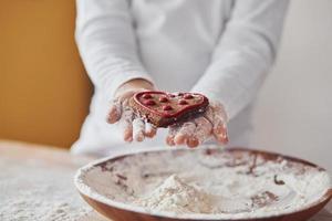 stänga upp se av liten flickans händer den där innehav ljuv kaka på de kök med tallrik av mjöl foto