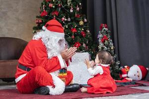 litet barn bebis flicka är har roligt spelar med santa claus i de rum fullt dekorerad och jul träd för säsong firande begrepp foto