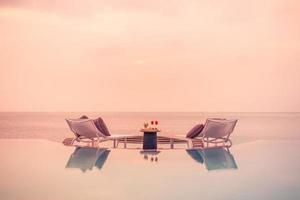 havsutsikt under solnedgångsljus med matbord med infinitypool runt. romantisk tropisk tillflyktsort för två, parkoncept. stolar, mat och romantik. lyx destination matsal, smekmånad mall foto