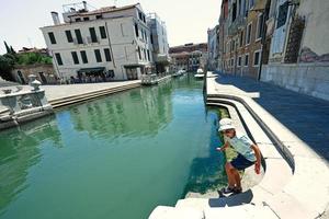 pojke i panama och solglasögon stå nära kanal i Venedig, Italien. foto