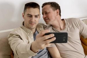 Lycklig Gay par med tillfällig kläder utgifterna tid tillsammans på Hem och framställning selfie på smartphone. homosexuell relationer och alternativ kärlek. mysigt interiör. foto