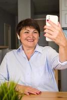äldre Lycklig kvinna innehav smartphone har videosamtal uppkopplad för talande med barn, vänner. lätt användande av modern teknologier.vertikal baner foto