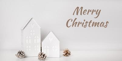 glad jul text med vinter- dekoration hus med lampor nära tall kottar.hälsningar kort foto