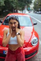 porträtt av Söt caucasian kvinna stående mot ny röd bil foto