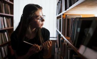 sökande för rätt information. mot fönster. kvinna studerande är i bibliotek den där full av böcker. uppfattning av utbildning foto