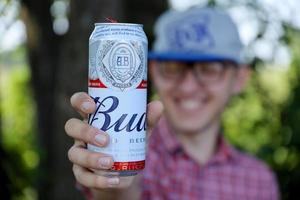 sumy, ukraina - augusti 01, 2022 ung man höja budweiser knopp öl kan och visar knopp logotyp på suddig flod och träd bakgrund. budweiser är ett av de mest populär öl märken i de USA foto