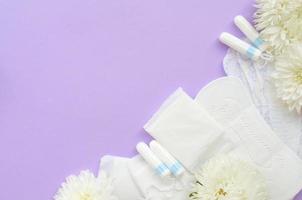 menstruations- dynor och tamponger med anbud vit blommor på pastell lila bakgrund foto