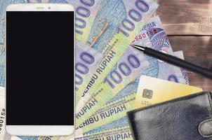 1000 indonesiska rupiah räkningar och smartphone med handväska och kreditera kort. e-betalningar eller e-handel begrepp. uppkopplad handla och företag med bärbar enheter foto