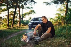 tid för en resten. man i svart skjorta nära de lägereld i de skog på hans helgen tid foto