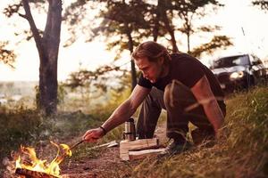 man i svart skjorta nära de lägereld i de skog på hans helgen tid foto