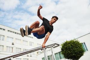 silver- färgad räcken. ung sporter man håller på med parkour i de stad på solig dagtid foto