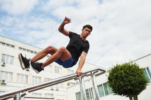 silver- färgad räcken. ung sporter man håller på med parkour i de stad på solig dagtid foto