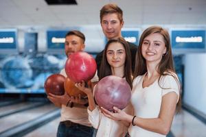 håller bollar i händerna. unga glada vänner har kul i bowlingklubben på sina helger foto