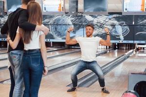 glad och visar muskler. unga glada vänner har kul i bowlingklubben på sina helger foto