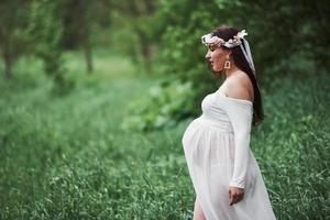 I förväntan. vacker gravid kvinna i klänning har en promenad utomhus. positiv brunett foto