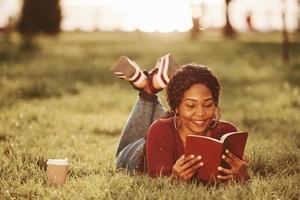 fullt koncentrering på läsning intressant bok. glad afrikansk amerikan kvinna i de parkera på sommartid foto