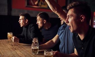 tre sporter fläktar i en bar tittar på fotboll. med öl i händer foto