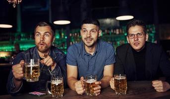 tre sporter fläktar i en bar tittar på fotboll. med öl i händer foto