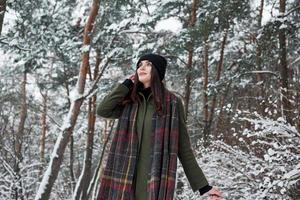 snöfall är kommande. glad ung flicka i värma kläder ha en promenad i de vinter- skog på dagtid foto