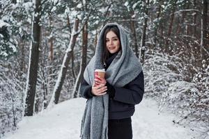 har Bra humör. flicka i värma kläder med kopp av kaffe ha en promenad i de vinter- skog foto