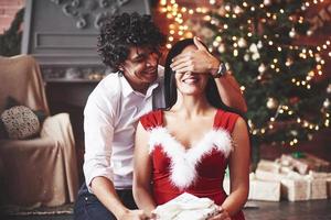 är du redo. kvinna i röd klänning beläggning henne ögon och kommer motta jul gåva från pojkvän foto