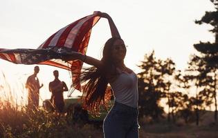 känner frihet. vänner ha trevlig helgen utomhus nära deras grön bil med USA flagga foto