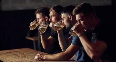 dricka öl. tre sporter fläktar i en bar tittar på fotboll foto