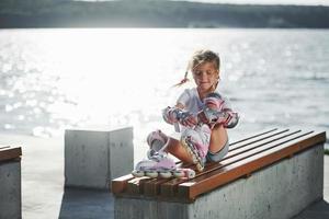 fixering henne skridsko vält. söt liten flicka utomhus nära de sjö på bakgrund foto