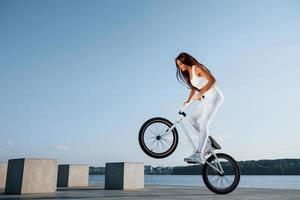 håller på med stunts. kvinna ryttare är på de cykel på dagtid nära de sjö. kondition kvinna i sportigt kläder foto