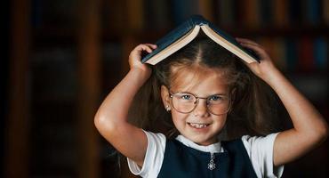 söt liten flicka i glasögon står i de bibliotek full av böcker. uppfattning av utbildning foto