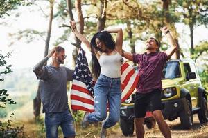 i de skog. vänner ha trevlig helgen utomhus nära deras grön bil med USA flagga foto