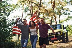 i de skog. vänner ha trevlig helgen utomhus nära deras grön bil med USA flagga foto