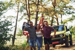 i de skog. vänner ha trevlig helgen utomhus nära deras grön bil med USA flagga foto